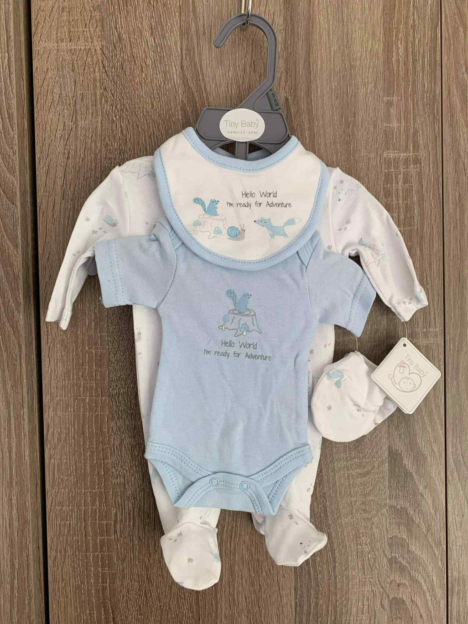 Baby clothing set with blue onesie, bib, and pants on a hanger against a wooden background.