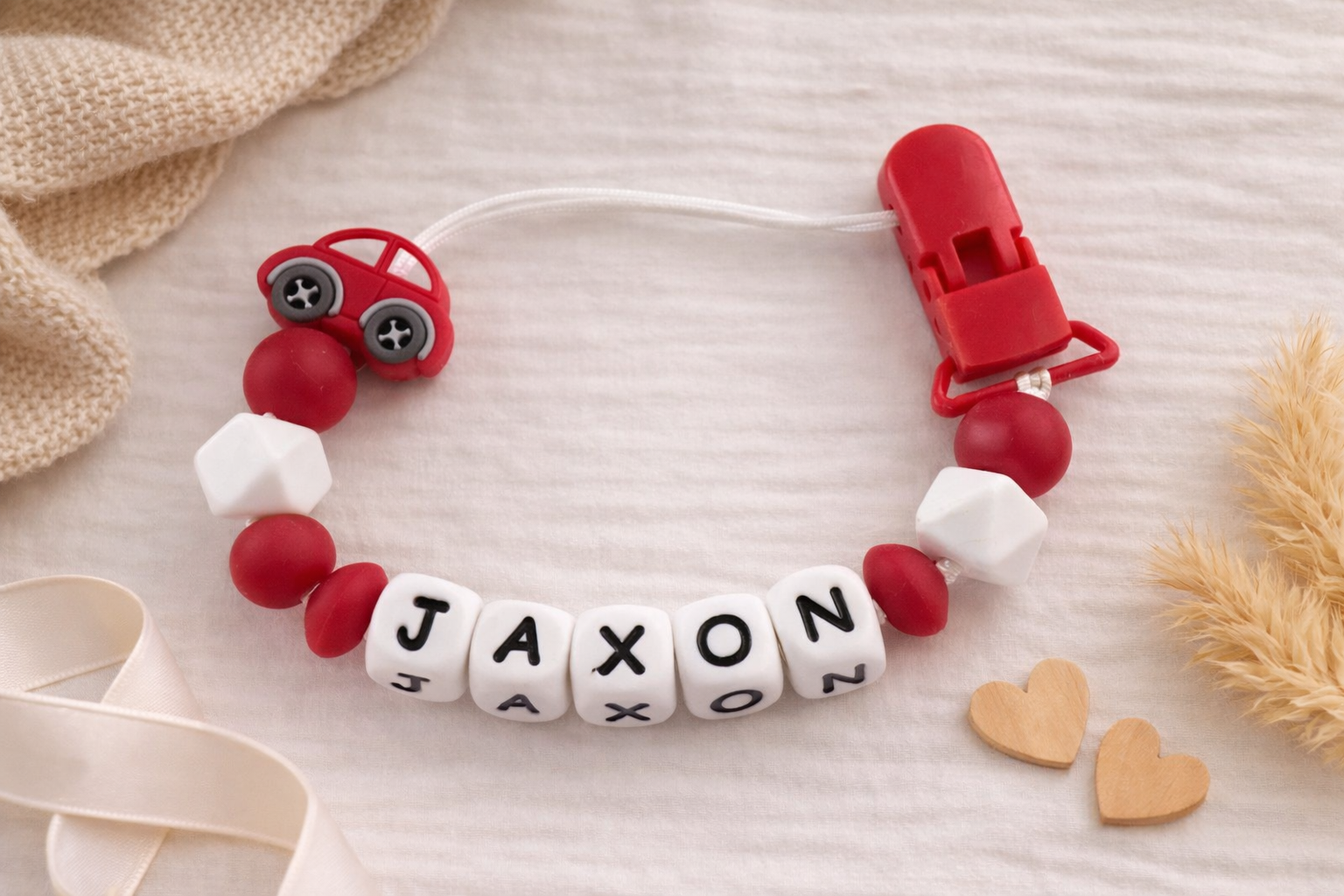 customised Red and white dummy clip with 'JAXON' on a beige background