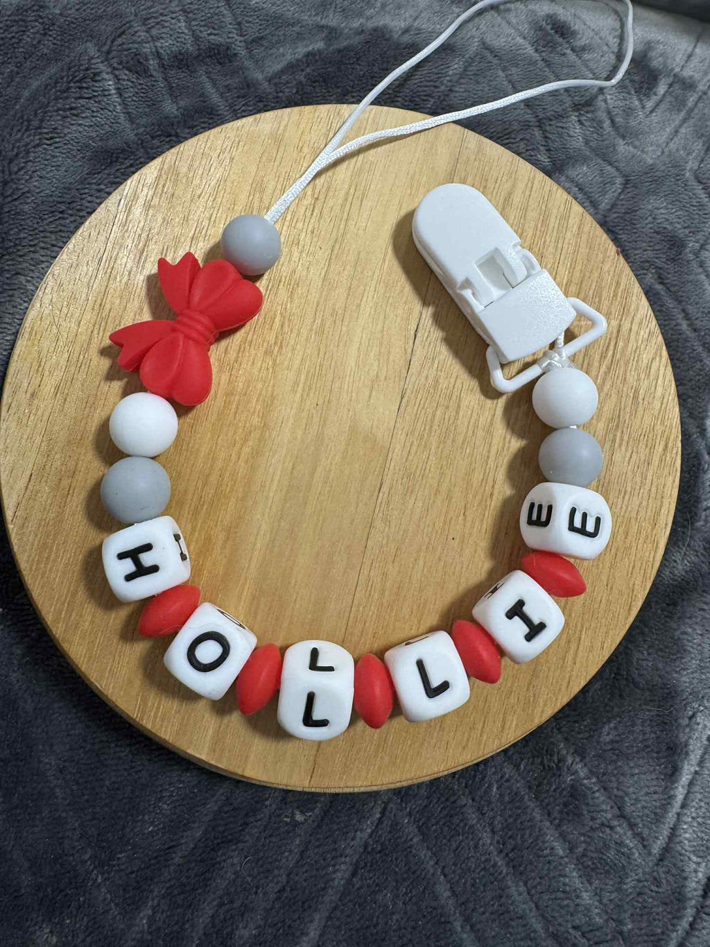 Personalized baby dummy clip with name 'HOLLIE' on a wooden board