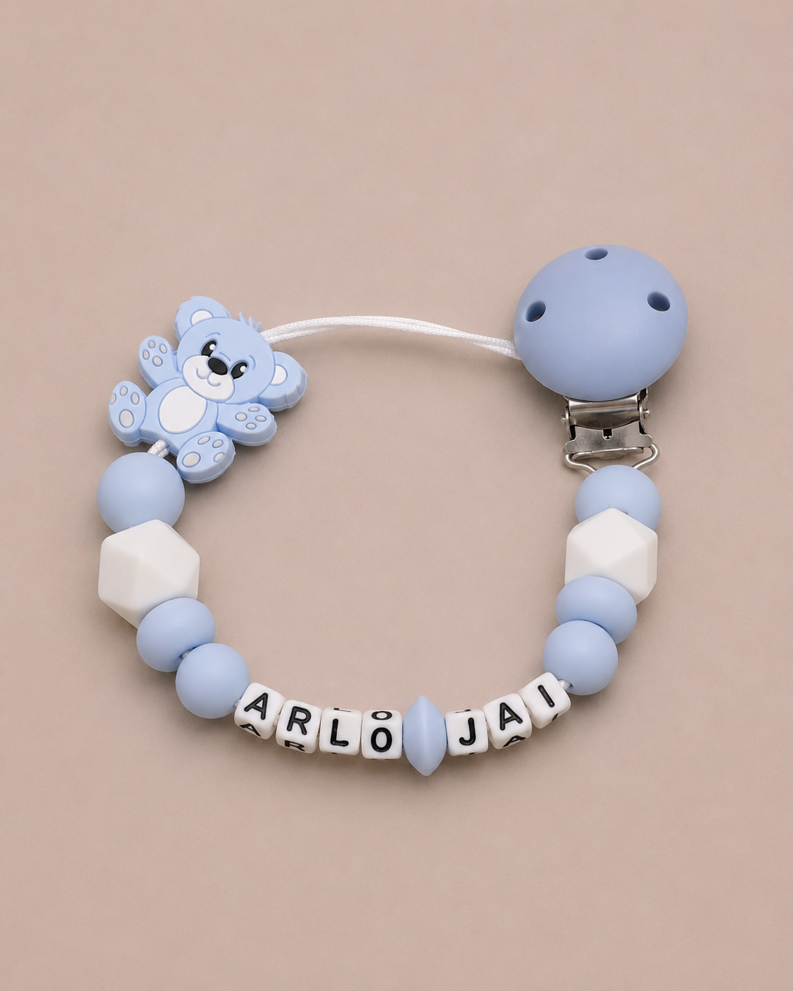 Blue and white dummy clip with bear design and name beads on a beige background