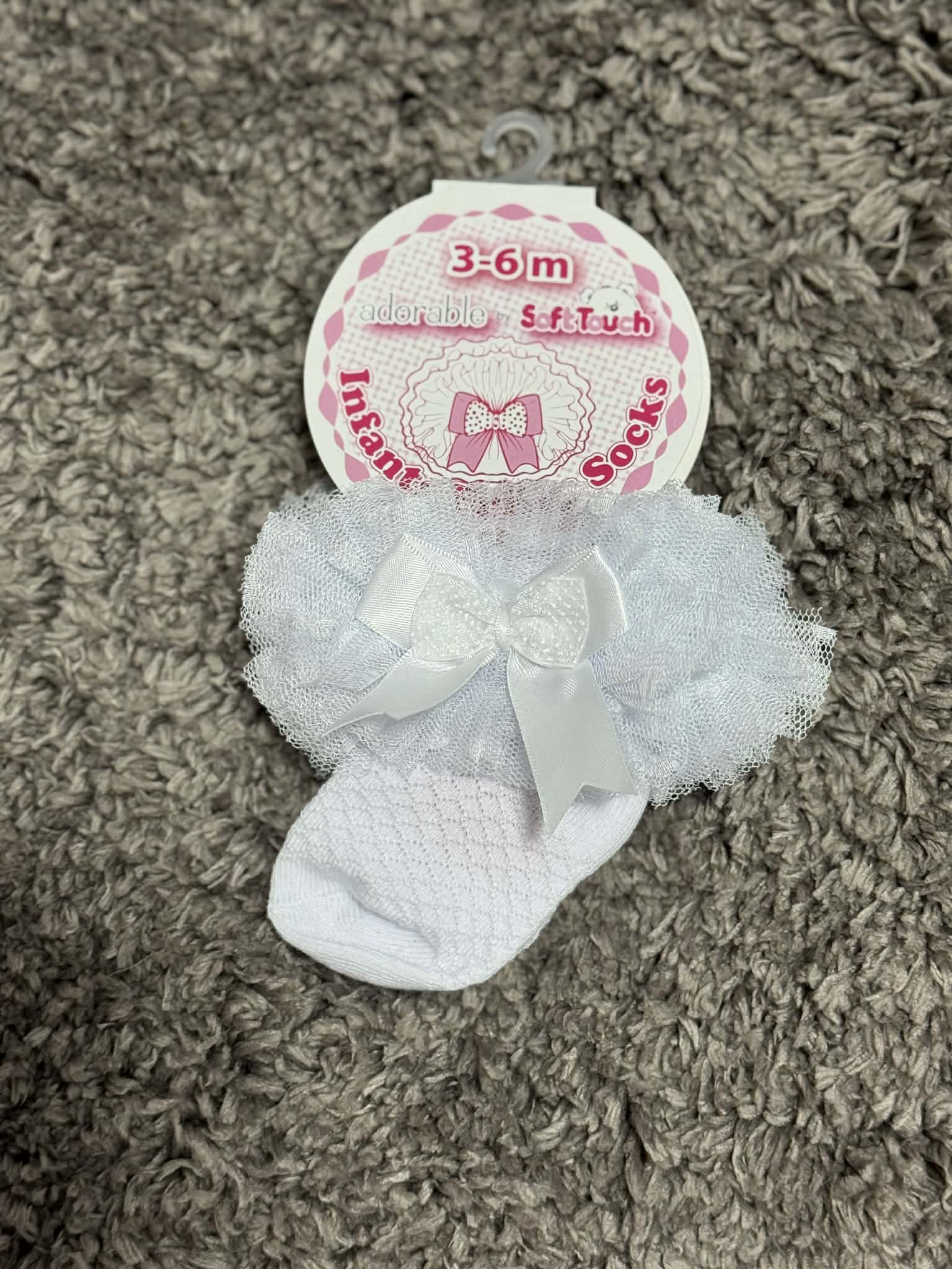 White baby socks with tulle and a bow on a textured surface