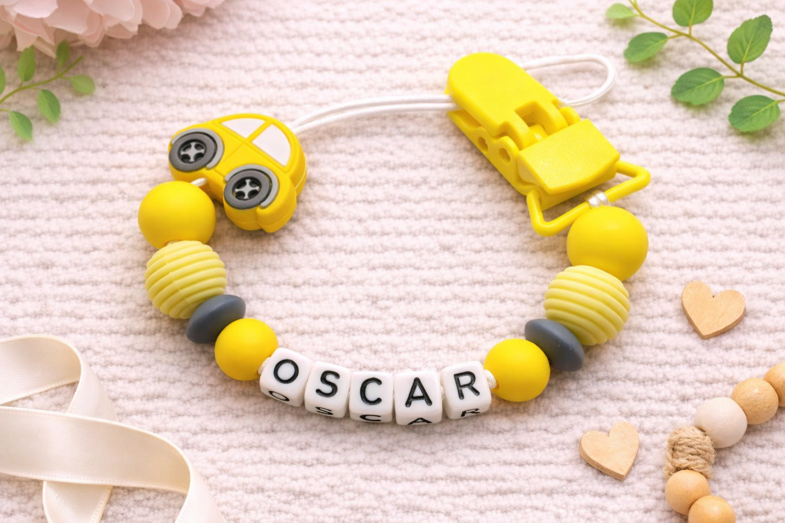 Yellow baby teether with 'OSCAR' beads on a soft fabric background