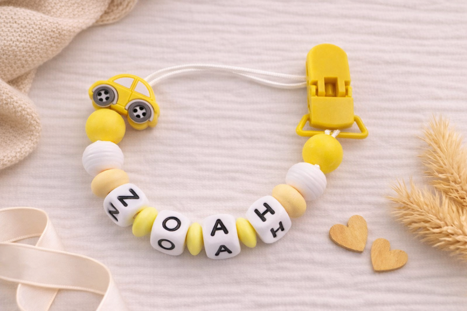 Yellow and white baby dummy chain with 'NOAH' letters on a light background