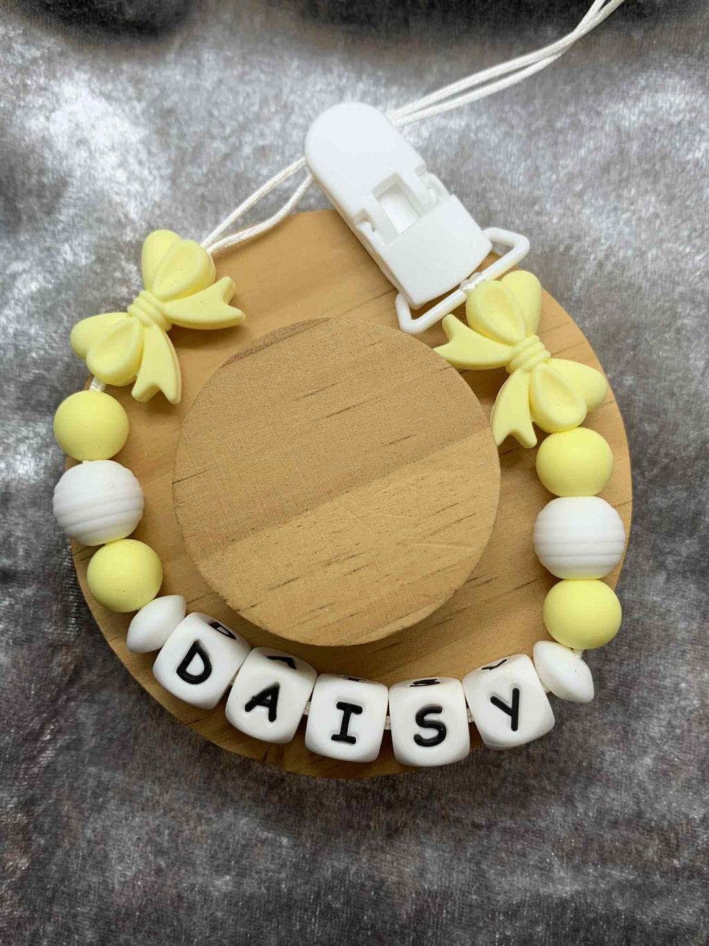 bow dummy clip with yellow and white beads spelling 'DAISY' on a gray background