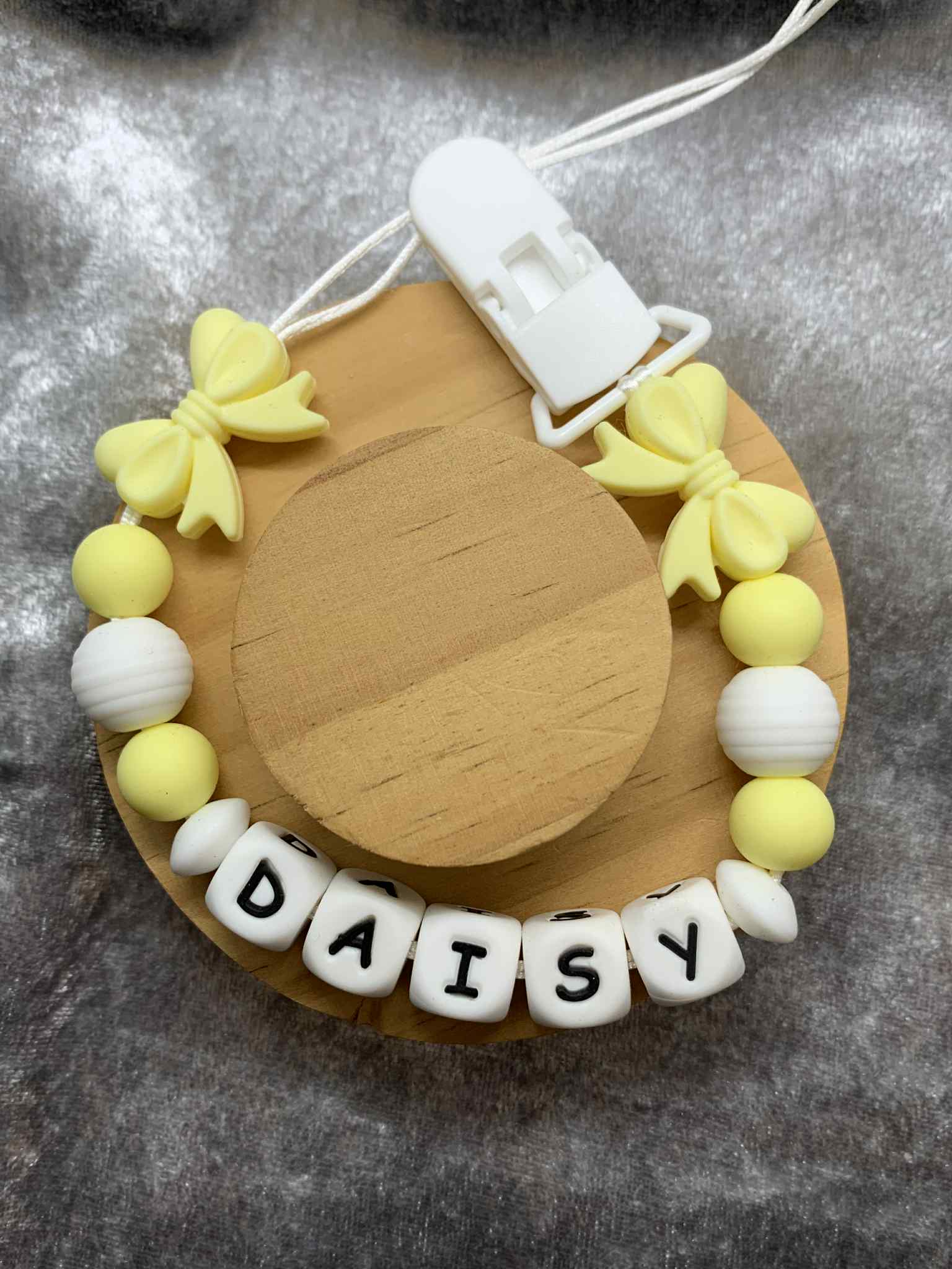 pacifier clip silicone with yellow and white beads spelling 'DAISY' on a textured surface